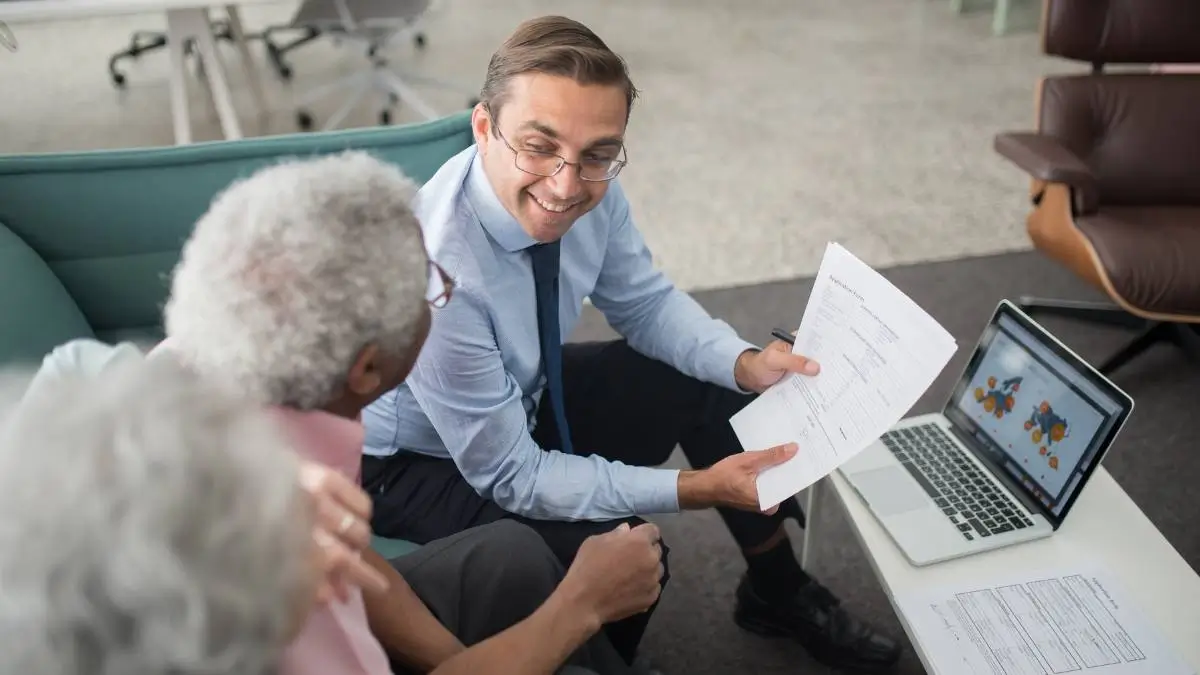 Conseiller présentant des documents à un couple lors d’un rendez-vous, pour illustrer des conseils stratégiques en assurance et prévoyance.