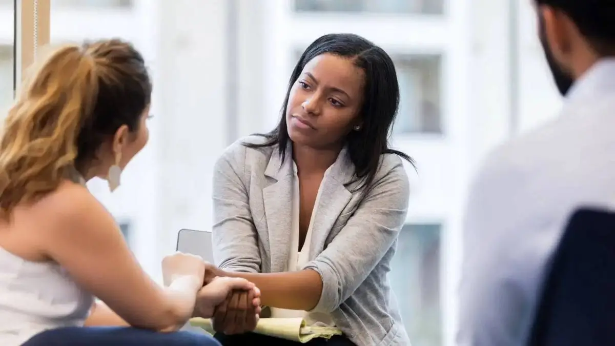 Conseillère attentive échangeant avec une cliente et lui tenant les mains, pour illustrer l’écoute client et la proximité dans l’accompagnement du cabinet Basile Debec.