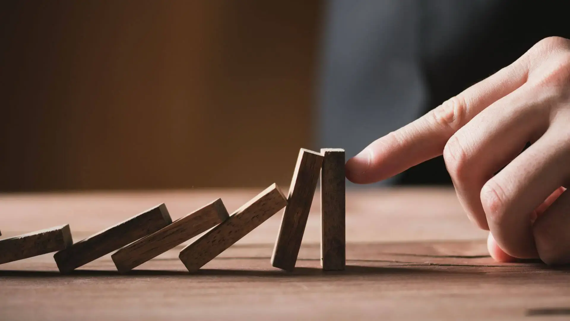 Main arrêtant une chaîne de dominos en train de tomber, pour illustrer la maîtrise des risques et la flexibilité dans un projet de financement.