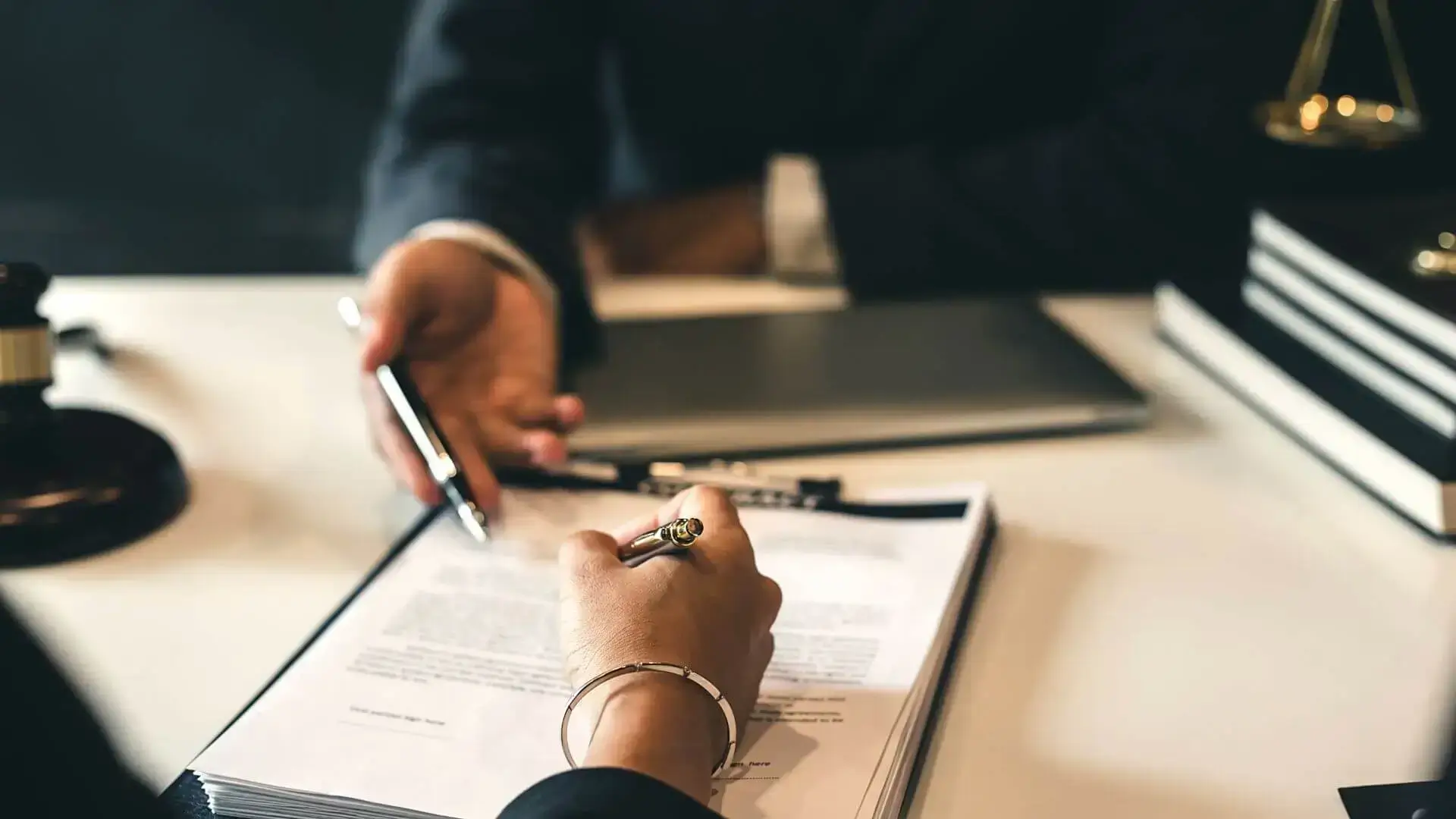 Personne signant un dossier pendant qu’un professionnel indique un document, pour illustrer le montage et la négociation d’un dossier de financement.