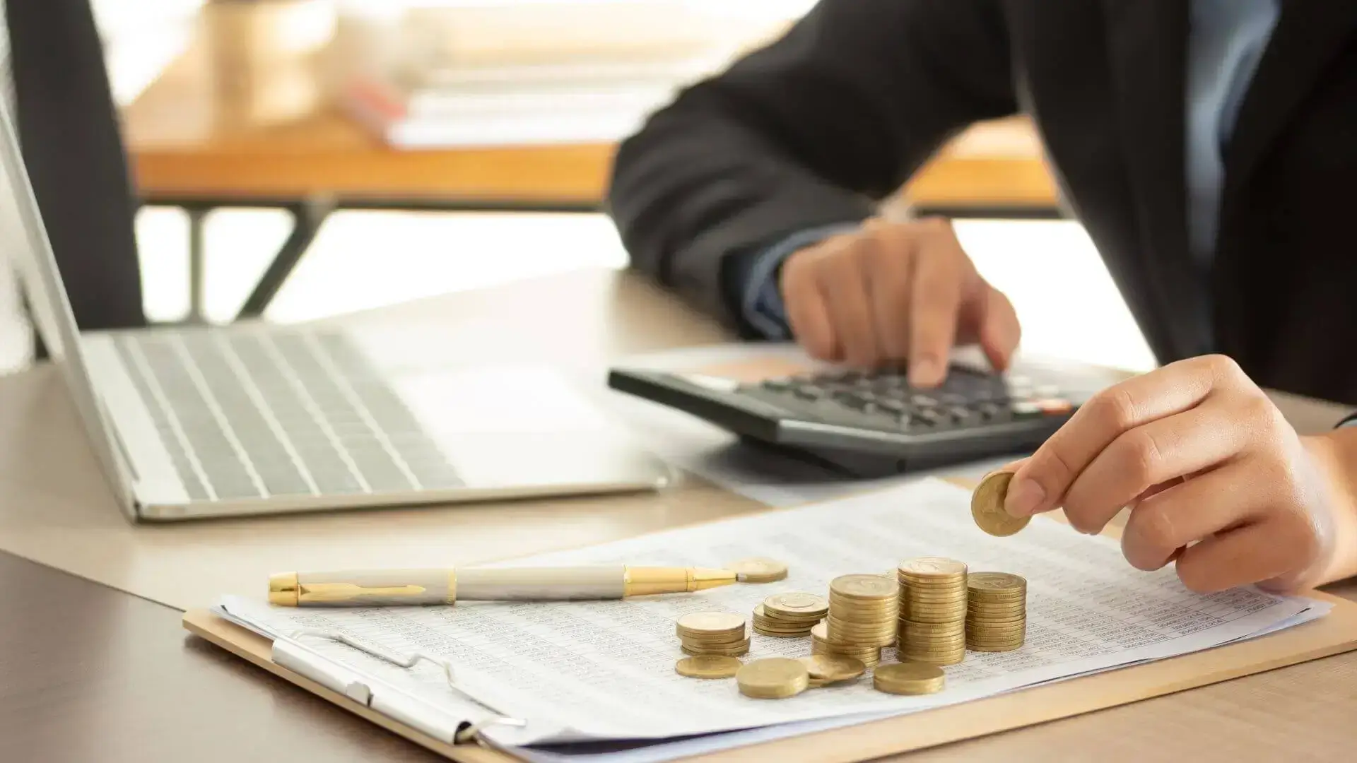Personne manipulant des pièces devant un ordinateur portable et une calculatrice, pour illustrer l’optimisation des ressources dans un projet de financement.