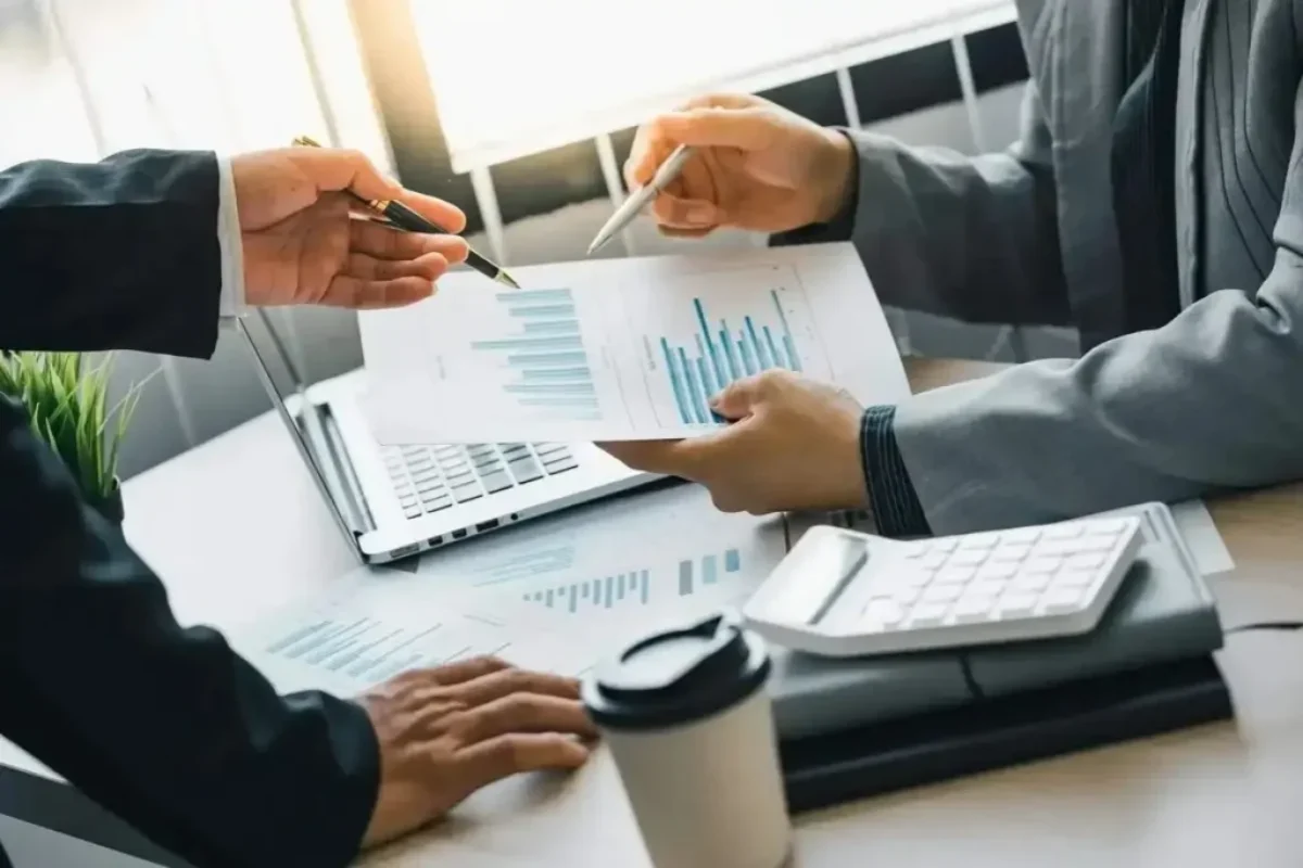Deux professionnels analysant des graphiques financiers sur des documents, avec un ordinateur et une calculatrice, pour illustrer des conseils en placements financiers.
