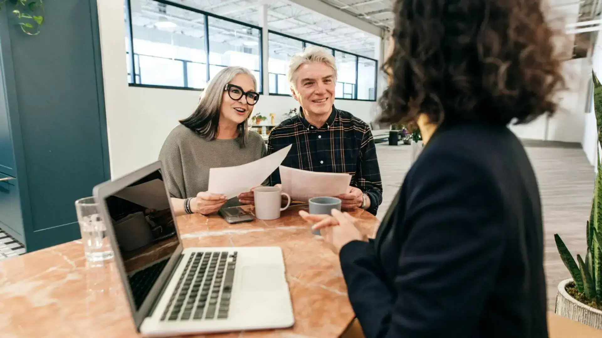 Couple en rendez-vous avec une conseillère, échangeant autour de documents, pour illustrer la planification successorale.