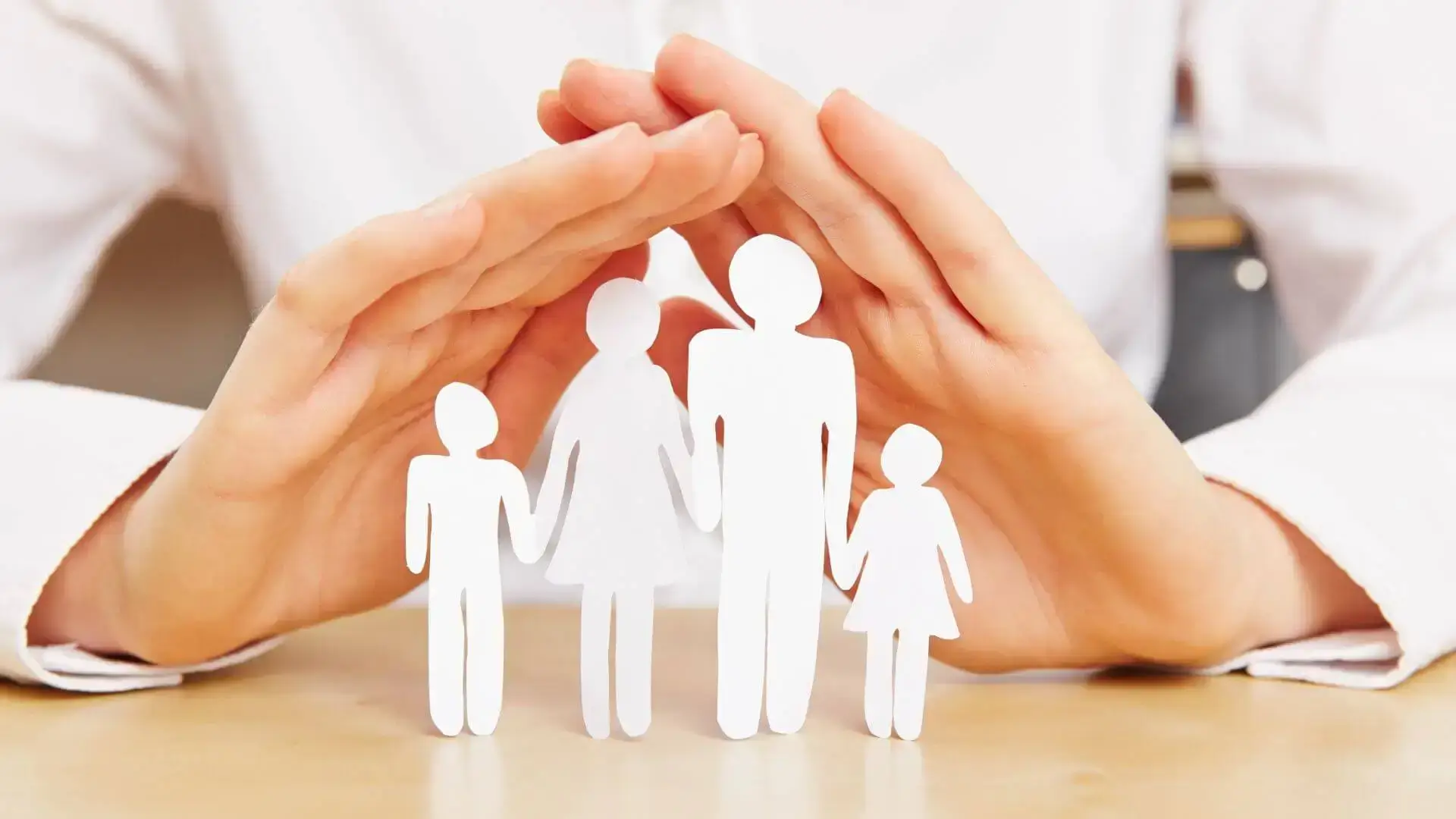 Mains protectrices autour de silhouettes représentant une famille, pour illustrer la protection financière des proches en assurance et prévoyance.