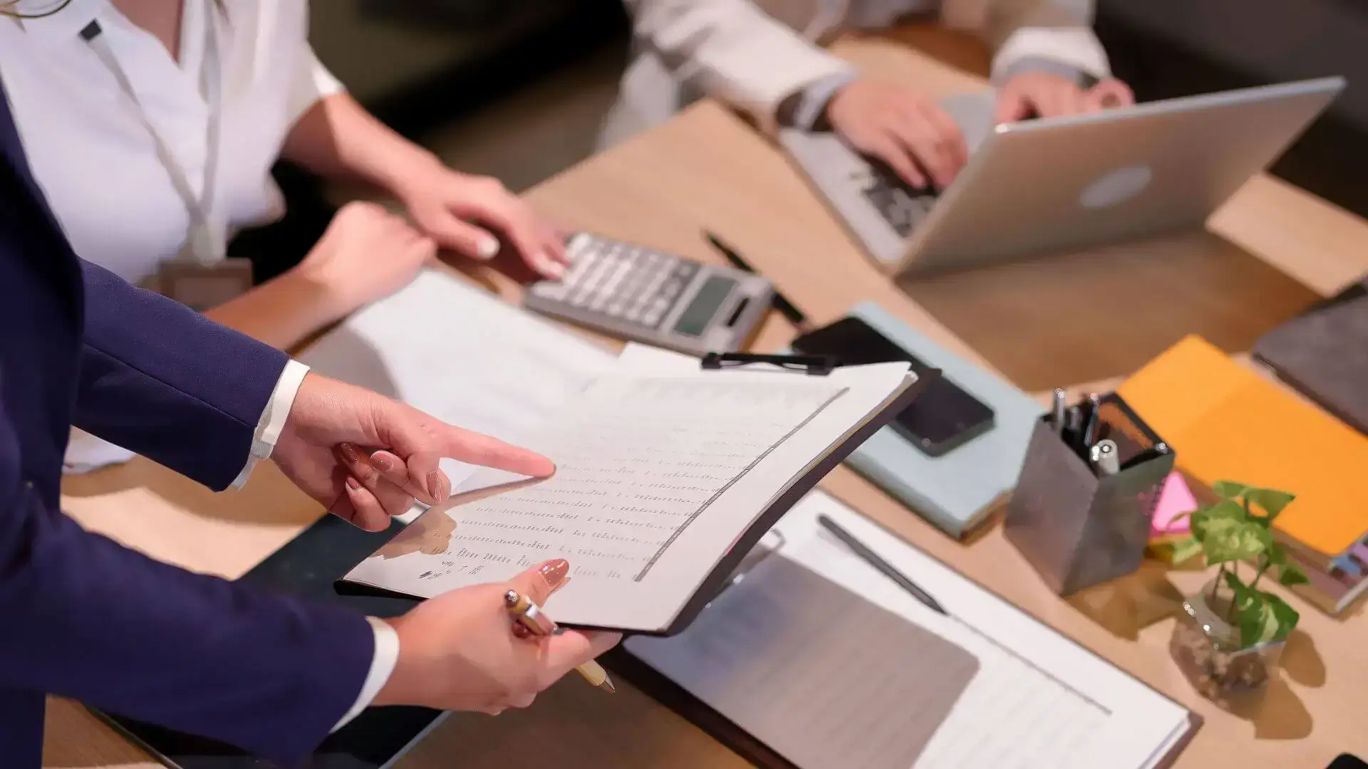 Professionnels examinant des documents de financement autour d’un bureau avec ordinateur portable et calculatrice, pour illustrer le suivi et l’ajustement des solutions.
